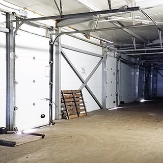 На фото: часть производственного помещения складского типа, полы - бетонная стяжка, помещение выполнено из металлоконструкций, обшитых сендвич-панелями и металлопрофилем, в левой стене установлены несколько роллетных ворот